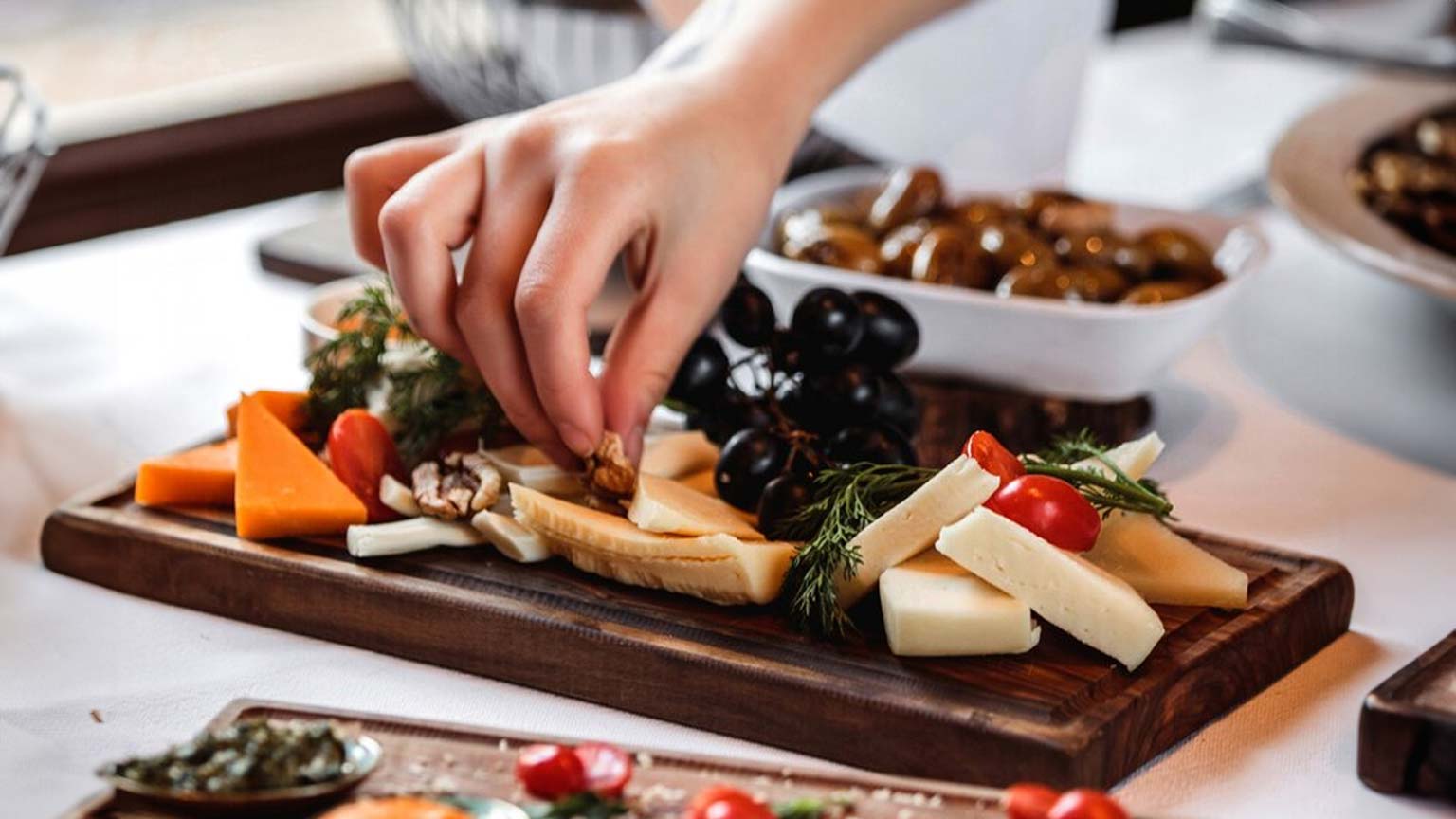 Una persona taglia formaggio e altri alimenti su un vassoio di legno, durante un evento di catering a km 0