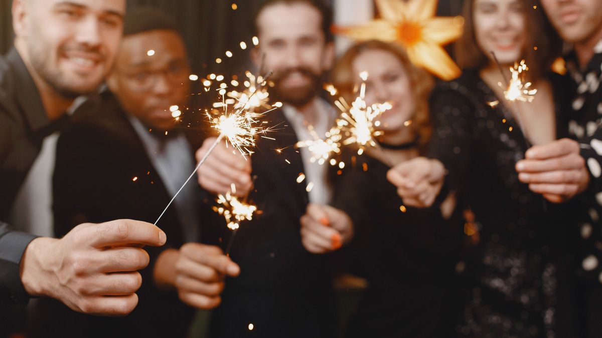 . Un gruppo di persone festeggia il Capodanno, tenendo in mano dei fuochi d'artificio scintillanti a una festa.
